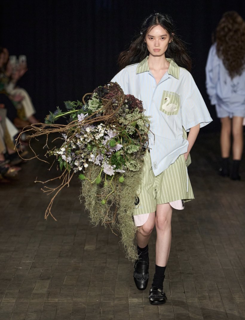 A model carrying a large floral bouquet in the Aknvas SS27 runway show