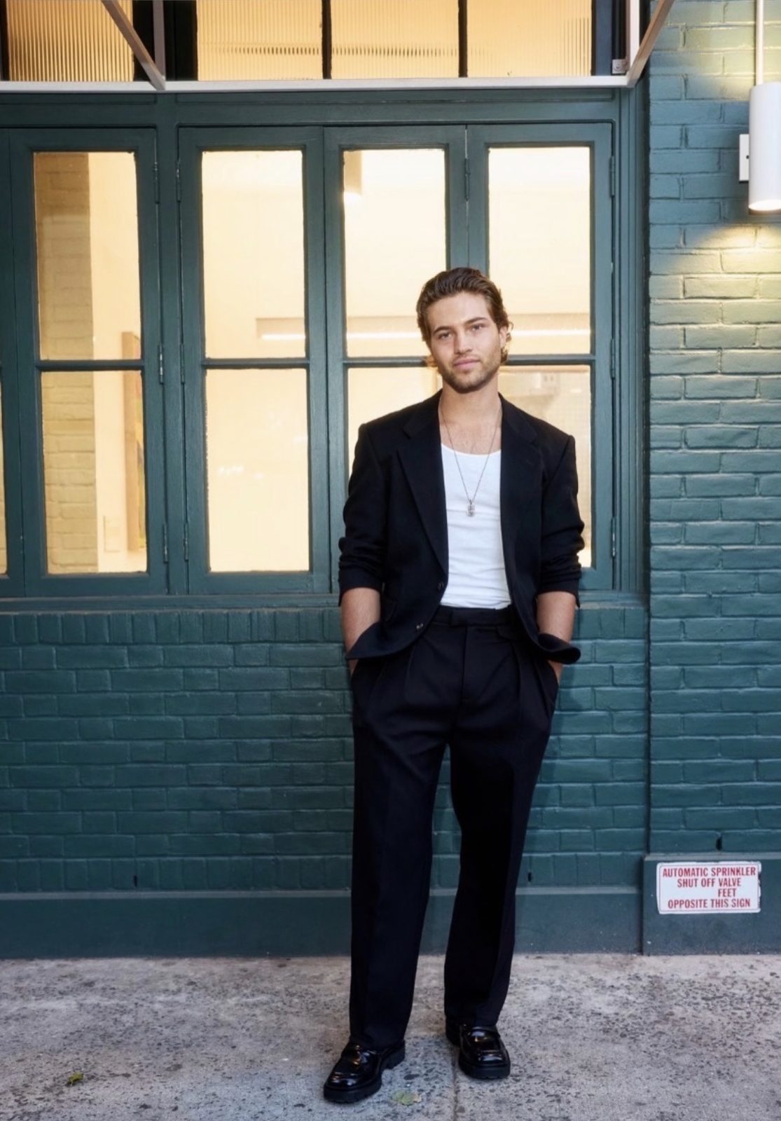 TJ Palma in a Select Vintage black suit and white tank in front of a green brick wall
